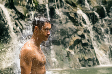 A defocused man hidden with streams of water standing under shower of tropical waterfall. Meditation in the wild nature