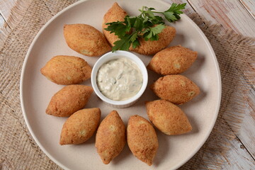 Deep fried kibbeh of ground beef meat mixed with bulgur, stuffed with fried minced meat with pine nuts on a clay plate on wooden table