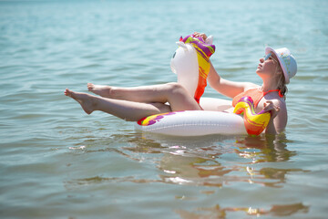 woman in a hat and sunglasses floats on an inflatable unicorn in the sea. enjoying the rest. advertising beach, sea recreation concept
