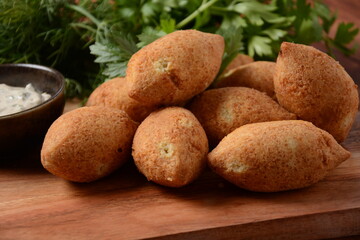 Deep fried kibbeh of ground beef meat mixed with bulgur, stuffed with fried minced meat with pine nuts on a clay plate on wooden board
