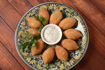 Deep fried kibbeh of ground beef meat mixed with bulgur, stuffed with fried minced meat with pine nuts on a clay plate on wooden table