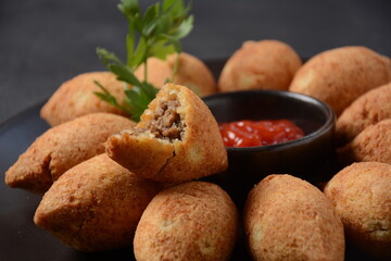 Deep fried kibbeh of ground beef meat mixed with bulgur, stuffed with fried minced meat with pine nuts on cutting board on dark background