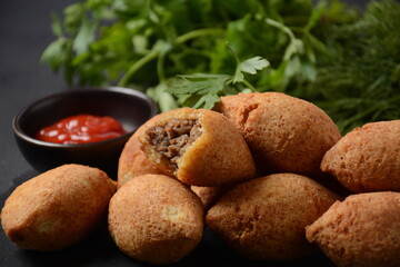 Deep fried kibbeh of ground beef meat mixed with bulgur, stuffed with fried minced meat with pine nuts on cutting board on dark background