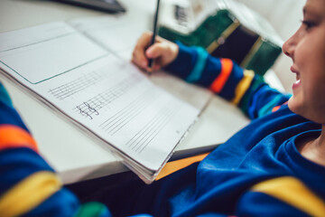 Little boy writes musical notes and violin key at home.