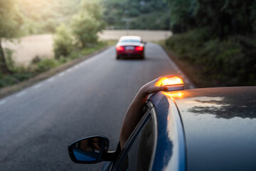 hand placing the new V16 emergency light, which replaces the emergency triangles, broken blue vehicle stopped on the road and with another car in the background