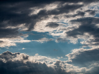 Fototapeta na wymiar Dramatic sky, clouds in with white and grays in the shadows. In the center a hole with blue sky.