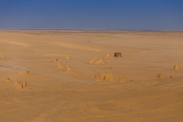 Fototapeta na wymiar Sandstone rocks with mirage on the horizon and wooden hut in the Sahara desert