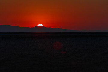Naklejka na ściany i meble Scarlet sunrise on the large endorheic salt lake Chott el Djerid in the Sahara desert of southern Tunisia with the Atlas Mountains on the background