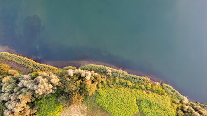 Naklejka na ściany i meble Aerial view of a picturesque place where transparent turquoise water of a forest lake meets a stony shore with trees in spring. captured with a drone. High quality photo