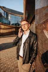 Handsome man with glasses with a smartphone on the street of a big city. Businessman talking on the phone on urban background