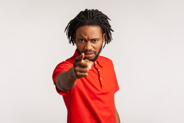 Portrait of angry bearded man with dreadlocks wearing red casual style T-shirt, pointing finger at...
