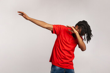 Portrait of young adult man with dreadlocks wearing red casual style T-shirt, standing in dab dance...