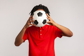 Unknown man with dreadlocks wearing red casual style T-shirt, hiding behind soccer ball, football...