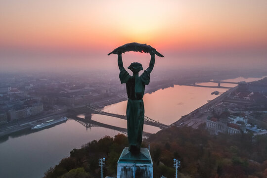 Aerial view to the Statue of Liberty with Liberty Bridge and River Danube at background taken from Gellert Hill on sunrise in fog in Budapest, Hungary