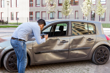 Side view portrait of man wearing jeans and shirt making photo of damaged car after auto accident,...