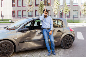 Fototapeta na wymiar Bearded man standing with grumpy face and showing loser gesture, upset over dented auto after road accident, wearing jeans and shirt, has upset facial expression. Outdoor shot.