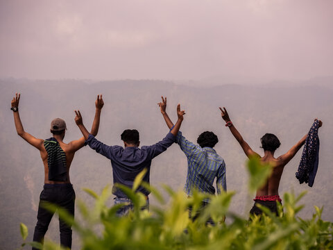 Silhouettes of Group of four happy friends is enjoying and having fun at mountain top , stands at breath taking view point and waving victory or peace sign and raising hands. Travel and tourism.