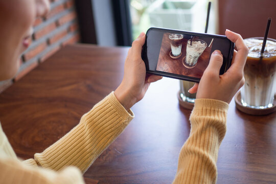 Woman's hand is taking a picture of a coffee with a smartphone. Women are taking photos to post or share popular dishes for social media.