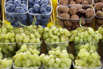 Fresh white grapes, plums and walnuts in plastic bowls for sale. Healthy eating