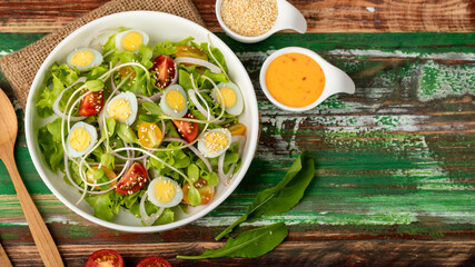 Big white bowl of lettuce, sprout salad with boil egg, and tomato mix with sesame dressing on sack cloth above wooden table with wood utensil, small olive oil jar and sesame cup. Concept for healthy