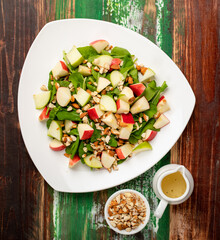 Healthy vegetarian rocket salad with dices apple, and chop almond in white dish place on colourful wooded table.  Concept for healthy