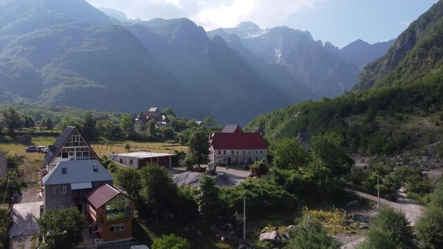 Flying near old wooden church and trees in Thethi valley, Albania. Aerial View of Theth National Park, Albanian Alps. Village, river and rocky mountains on the background.