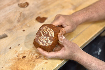 Hands of a ceramist who cuts a cup made in Japanese technique Nerikomi from red and light clay to develop the pattern