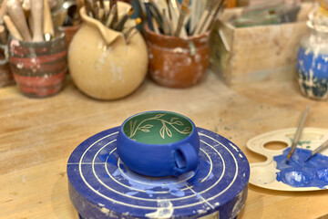 Painted blue and green cup made on a potter's wheel dries on a turntable for painting