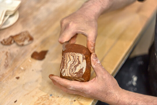 Hands of a ceramist who cuts a cup made in Japanese technique Nerikomi from red and light clay to develop the pattern