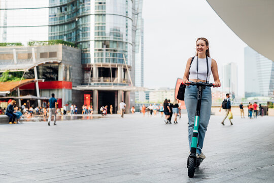 Young caucasian woman outdoor riding kick scooter smiling happy enjoying green transportation