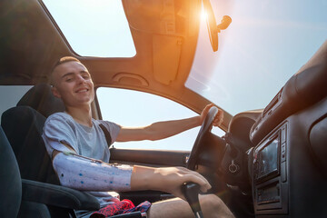 Young smiling caucasian man with amputated arm and prosthesis drives a car on a sunny day in summer. Side view inside of cabin - Powered by Adobe