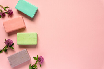 Flat lay of various natural soap bars with clover flowers on pink background. Space for text