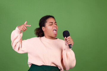 Beautiful african american woman on green background with microphone singing songs in karaoke with eyes closed