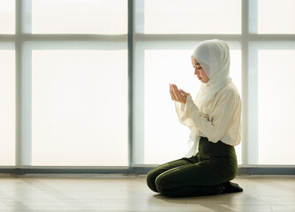 Young and beautiful Asian Muslim woman sitting on floor and praying with respect and calm manner