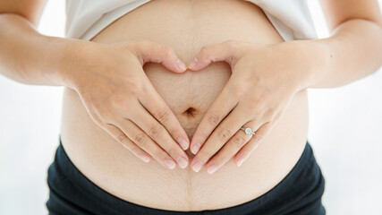 a picture of beautiful hands with a nice fair skin making a gesture of heart shape on pregnancy's belly over white background. Healthy and happy mother concept