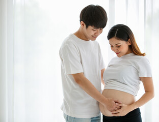 lovely young Asian couple husband and wife standing together smiling and touching a pregnant woman's belly with love and care. Happy and healthy family concept