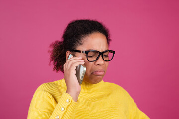 Beautiful african american woman on pink background having conversation on mobile phone unhappy crying