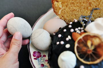 Easter eggs and buns decorated with slice of orange on a plate. An egg in a hand.
