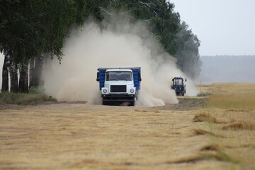 Russian truck and tractor fast drive on dusty road on harvested linen field edge, linum harvesting in Russia at summer day