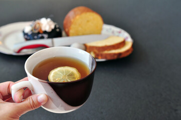 Cup of black tea with a slice of lemon in a hand and Easter buns on a plate with free space for your text