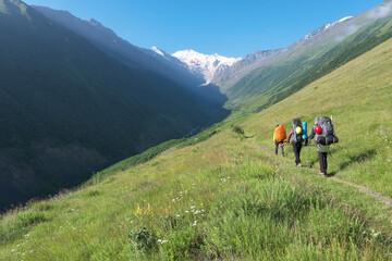 Fototapeta na wymiar Group of tourists (climbers) walk towards Mount Kazbek through Genaldon river gorge on sunny summer day. North Ossetia–Alania, Caucasus, Russia.