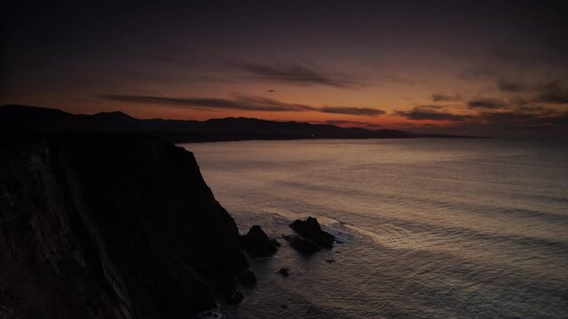 Timelapse. Sunset over rocky cliffs at Asturias coast in north Spain. View from Faro de Cabo Busto. Tourist attraction, place to visit.