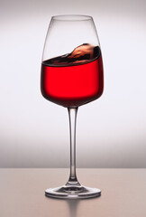 A close-up of crystal glass with red wine on the light background. Wavy surface, no splashes. Restaurant glassware, beverage, table setting, romance, passion, love, party, water splashes.