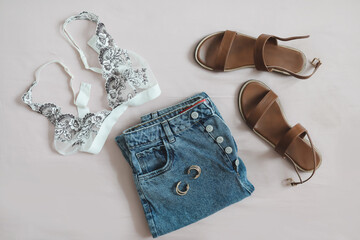 flat lay composition with female lingerie, denim shorts and sandals on beige background top view