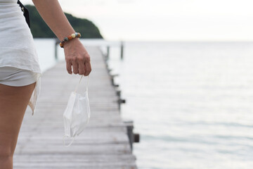 Asian female hand holding face mask with pier and sea