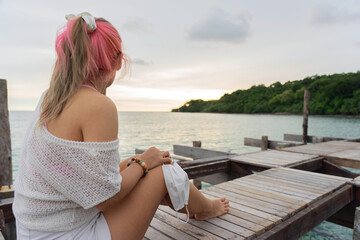 Asian woman holding face mask sitting on platform in sea