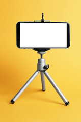 Modern tripod with smartphone on yellow background
