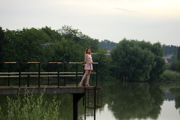 Portrait of beautiful woman in pink dress standing on a bridge at the lake