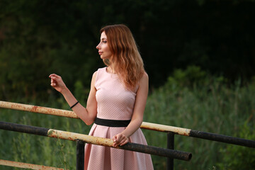 Naklejka premium Portrait of beautiful woman in pink dress standing on a bridge at the lake