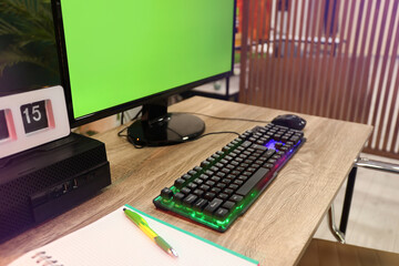 Modern computer and RGB keyboard on wooden table indoors. Mockup green screen